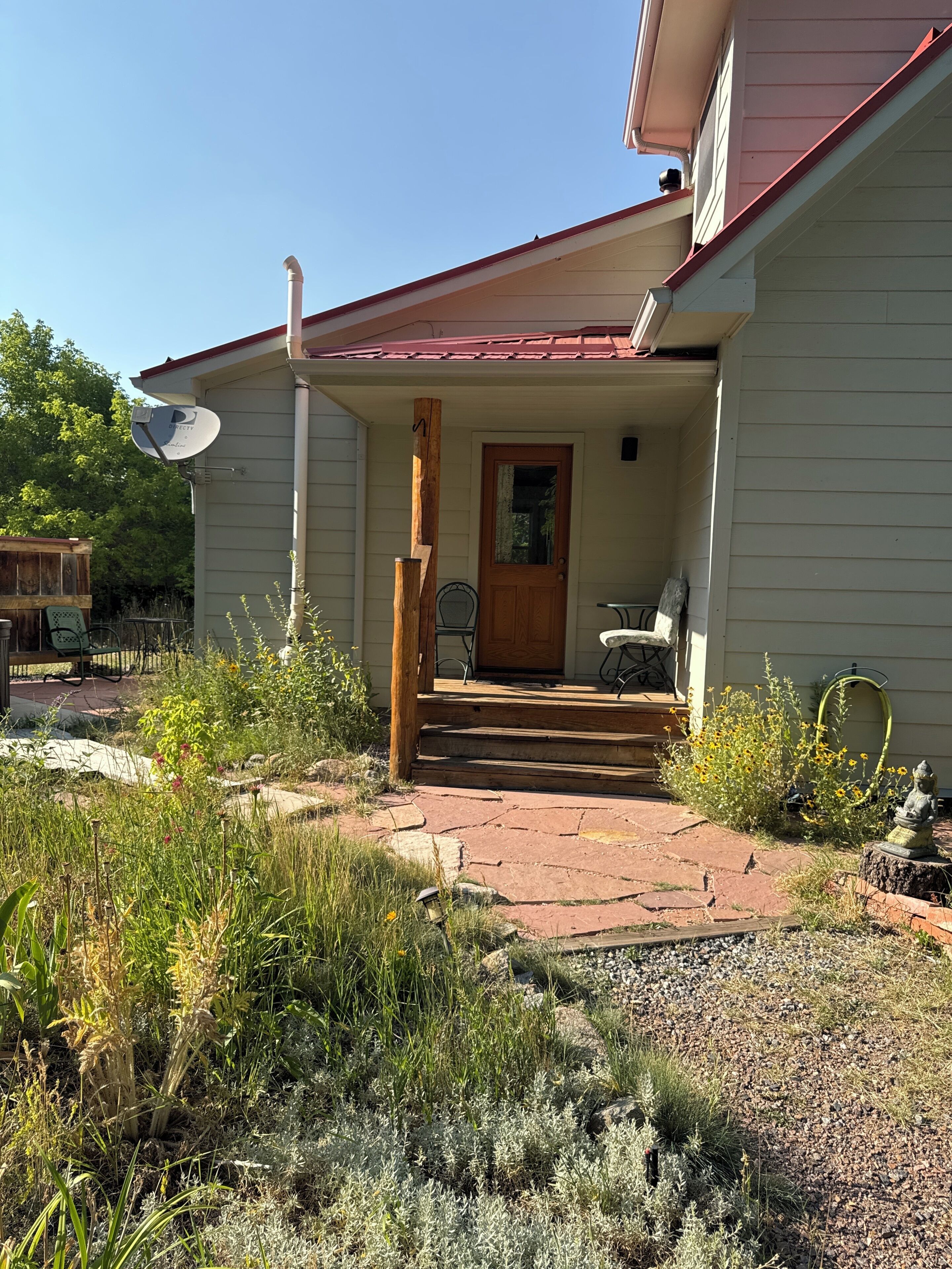 Ein Haus mit einer Veranda, einer Satellitenschüssel und einem Garten mit verschiedenen Pflanzen.