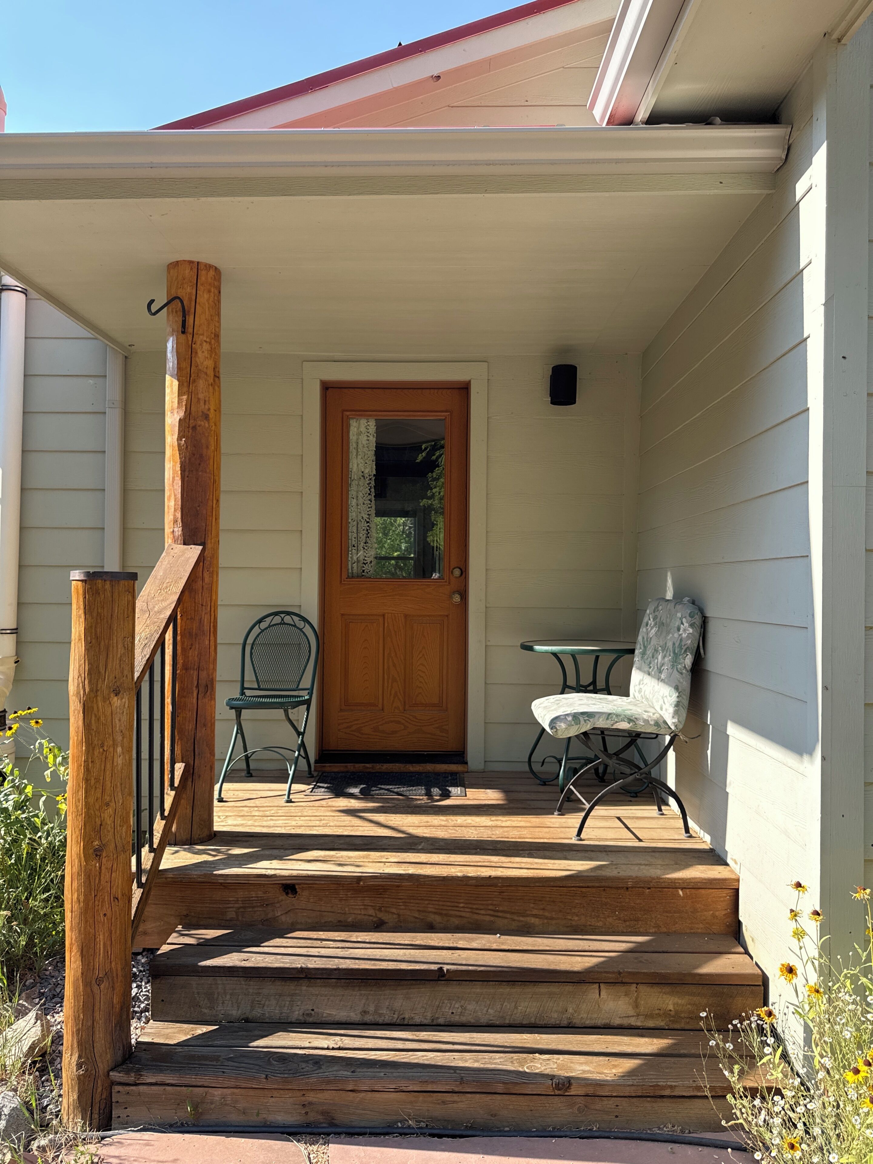A wooden staircase leading to a front door with a glass panel, two chairs, and a small table on a porch.