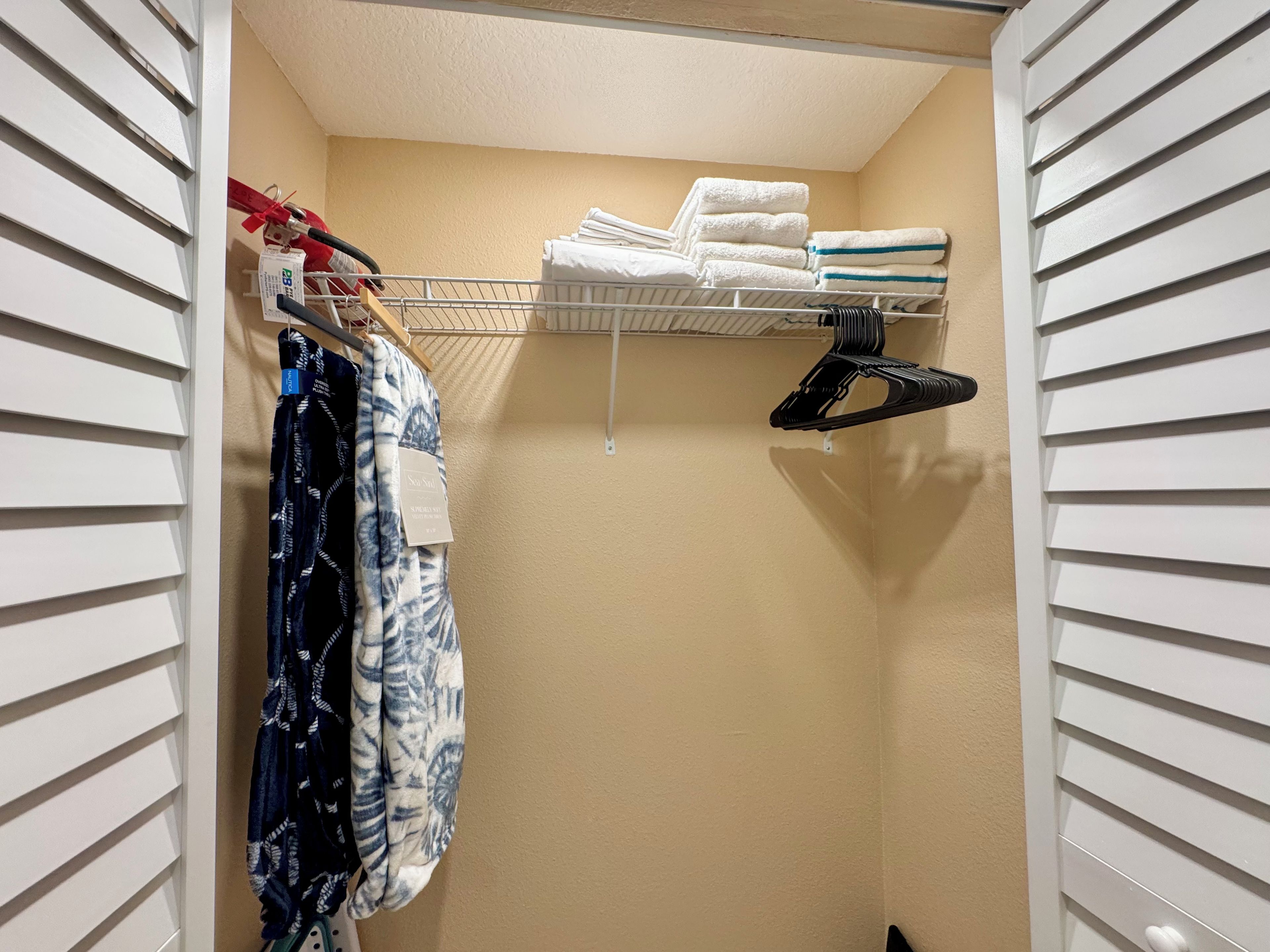 A closet with hanging clothes, a shelf with folded towels, and a shoe rack.