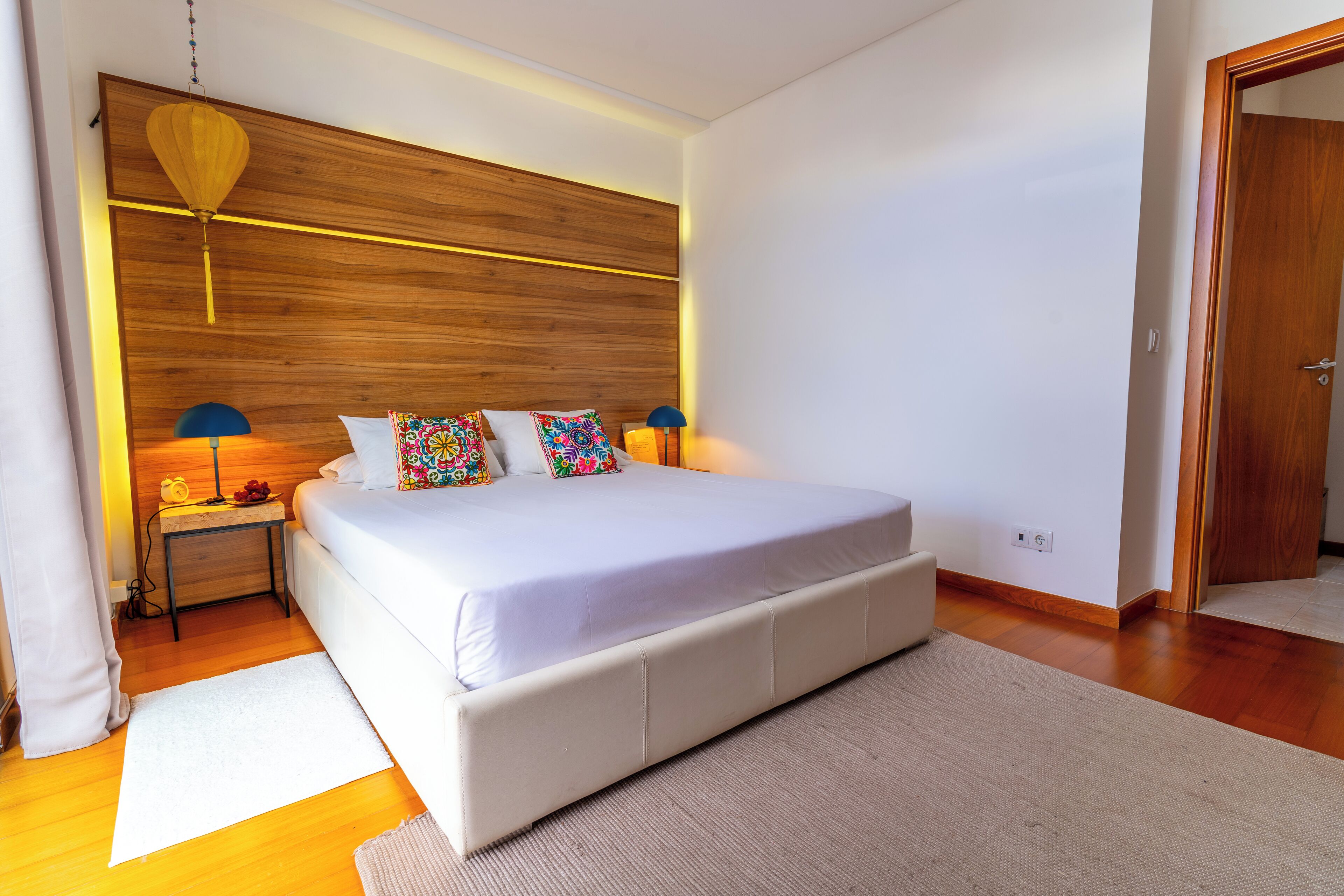 Een slaapkamer met een groot bed, een houten hoofdbord, bedlampjes en een deur.