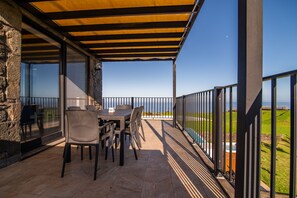 A covered outdoor patio with a table and chairs, stone walls, and a view of the sea. - House in countryside (Lomba da Fazenda)