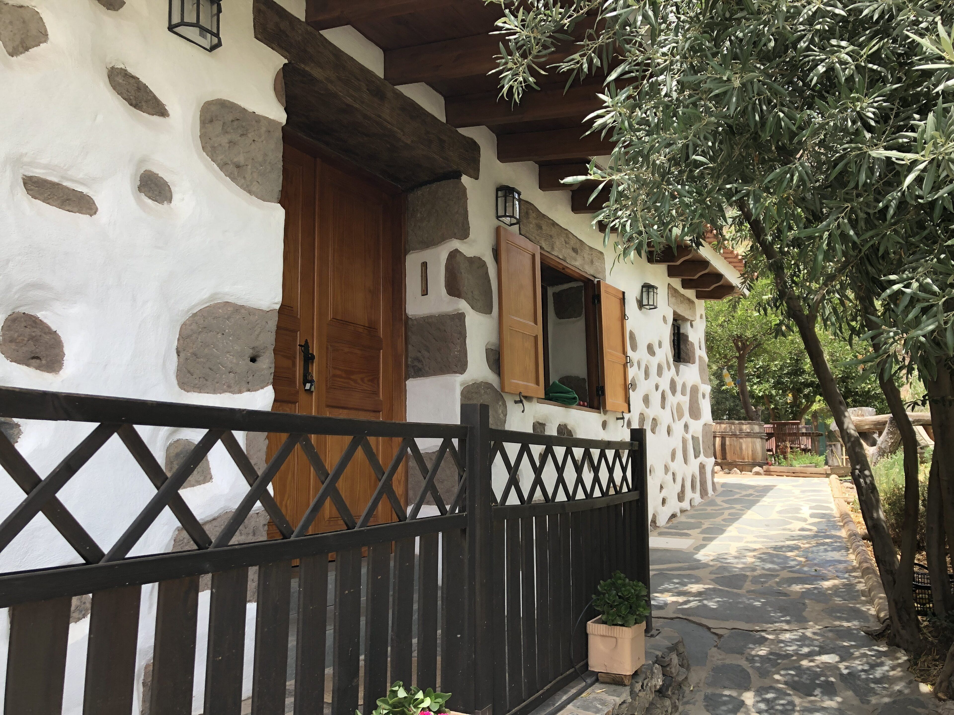 A stone building with a wooden door and window shutters, a black gate, and a potted plant.