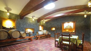Una bodega rústica con barriles de madera, paredes de piedra y un comedor con mantel a cuadros.