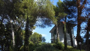 A white building with a sloped roof, surrounded by dense greenery and trees. - Torre Alpicella Holiday Home, a scenic escape into nature and relaxation! (Diano Marina)