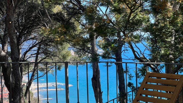 A balcony with a wooden table and chairs, overlooking a coastal area with trees and a clear blue sea. - Torre Alpicella Holiday Home, a scenic escape into nature and relaxation! (Diano Marina)