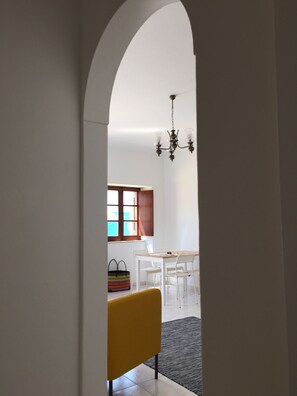 Une vue intérieure d’une pièce comprenant une table à manger, des chaises, un lustre et une fenêtre avec des rideaux.
