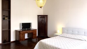 Une chambre à coucher avec un lit, un bureau avec une télévision, une armoire en bois et un lustre.