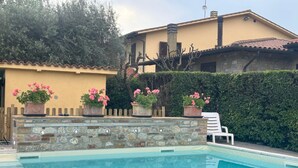 A swimming pool with stone walls, potted pink flowers, and a white chair. - **One bedroom Apartment “Pesci” – For 2–4 people** (Assisi)