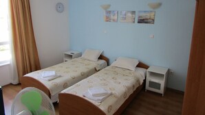Una habitación de hotel con dos camas individuales, una mesita de noche con lámpara, un reloj de pared y una ventana con cortinas.