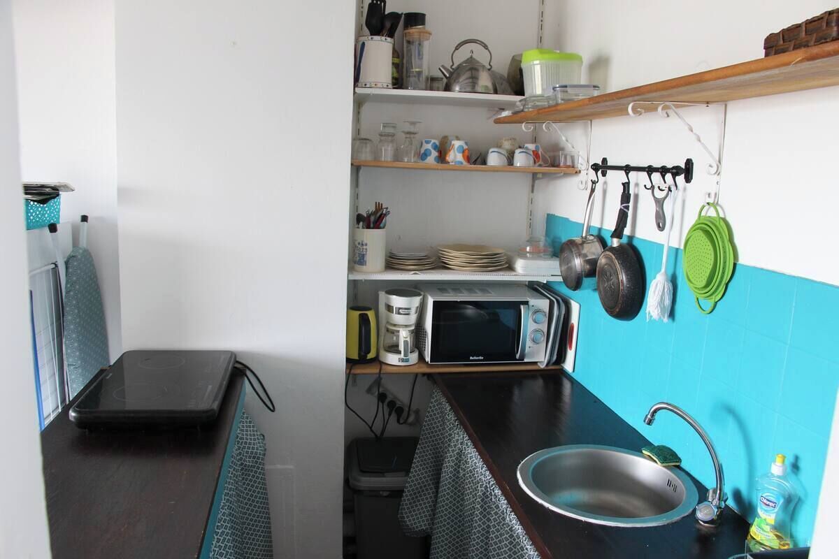 Cocina compacta con microondas, hervidor y diferentes utensilios en estantes.