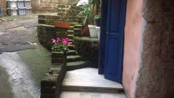 Un étroit sentier de pierres mène à un bâtiment doté d’une porte bleue, entouré de verdure et de murs de pierre.