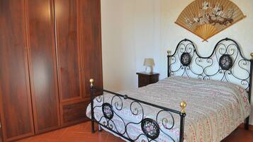 A bedroom with a wooden wardrobe, a bed with a decorative headboard, and a wall-mounted fan.