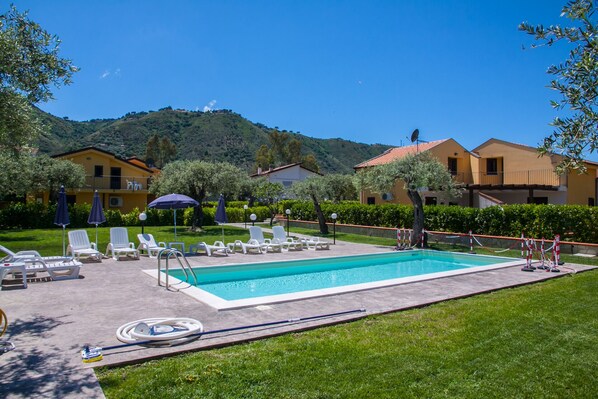 Una piscina con sillones de descanso, una manguera y montañas al fondo.