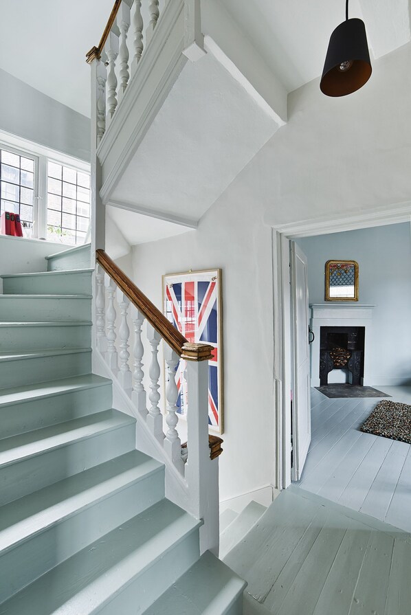 Un escalier avec des balustrades blanches et une main courante en bois, menant à une pièce dotée d’une cheminée et d’un tableau encadré au mur.