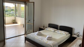 A bedroom with a bed, a nightstand, a lamp, and a view of the outside balcony. - Penthouse with Panoramic Veranda immersed in Nature, a stone's throw from the Ionian Sea (Badolato Marina)