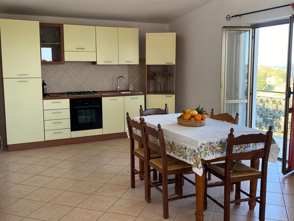 A kitchen with light yellow cabinets, a dining table with a floral tablecloth, and a fruit basket.