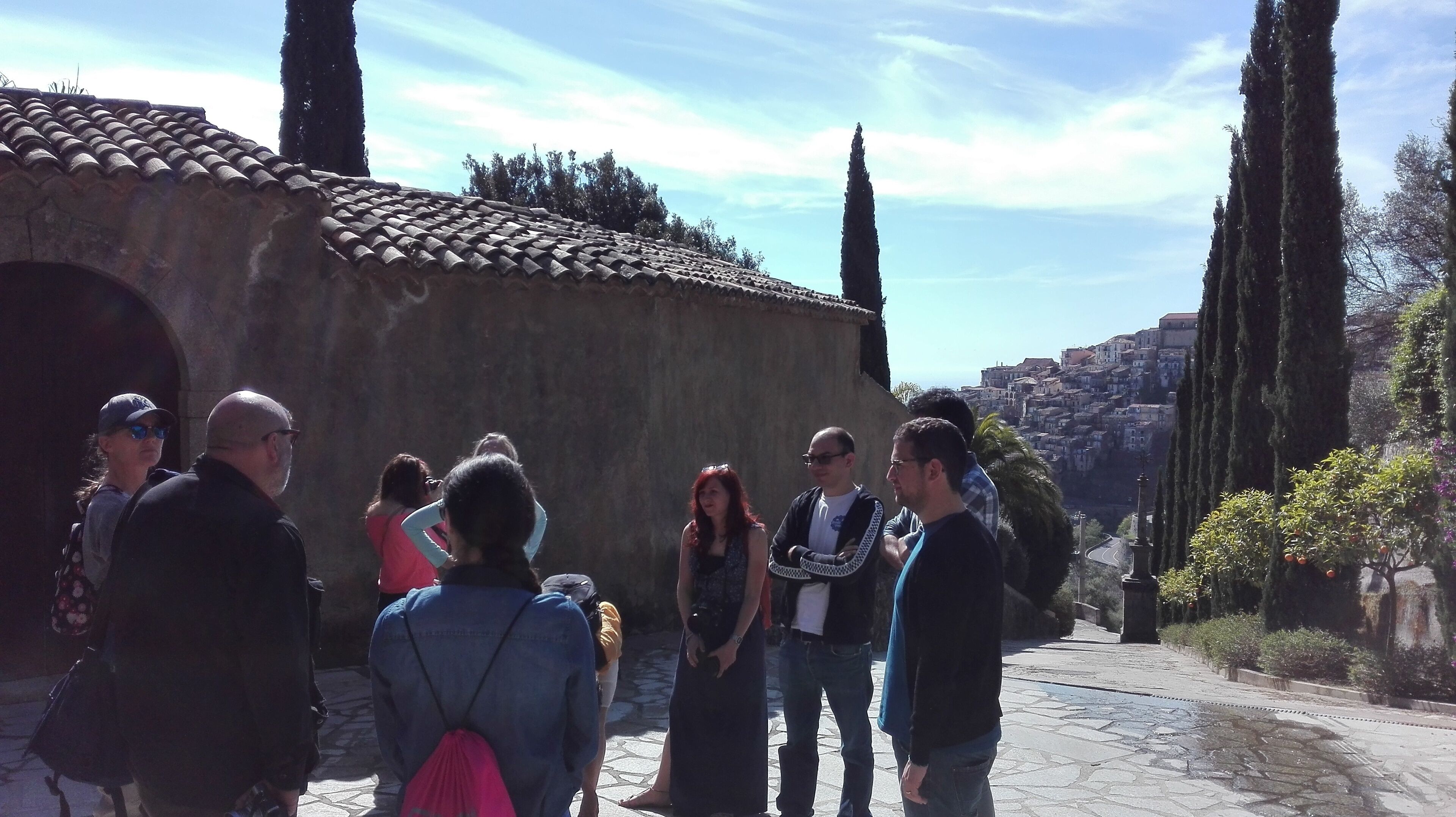 A group of people standing in a stone-paved area with a tiled-roof building in the background.