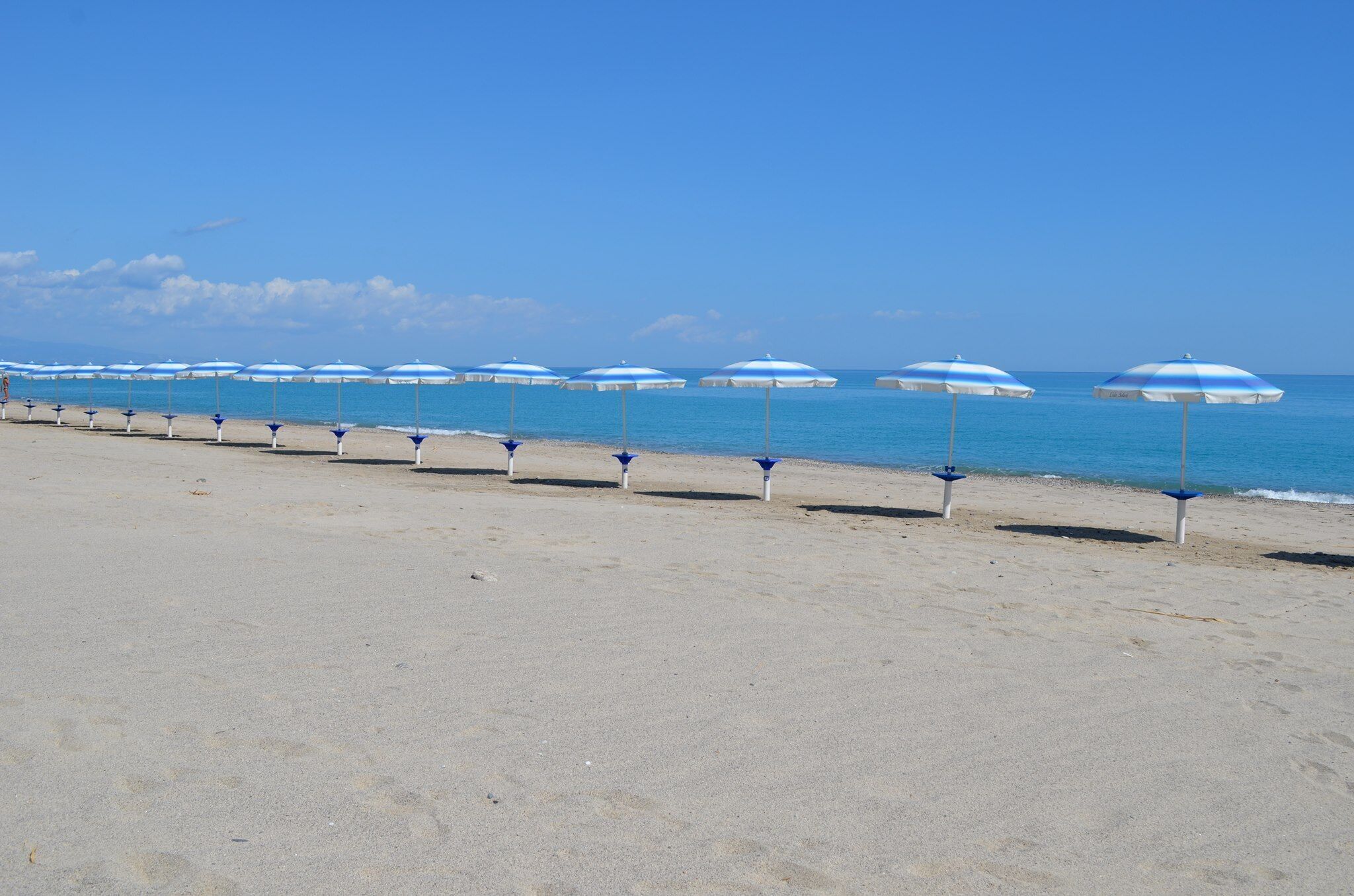 Une plage bordée de rangées de parasols bleus et blancs.
