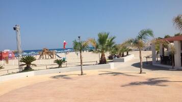 A beachside area with palm trees, a playground, and a building with outdoor seating.