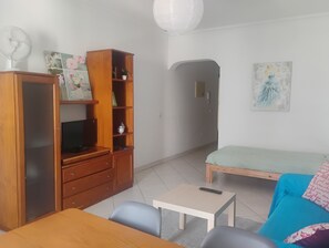 Une pièce comprenant un meuble en bois, une télévision, une petite table, un canapé et un tableau accroché au mur.