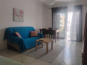Een woonkamer met een blauwe bank, een bijzettafeltje en een eethoek met stoelen.