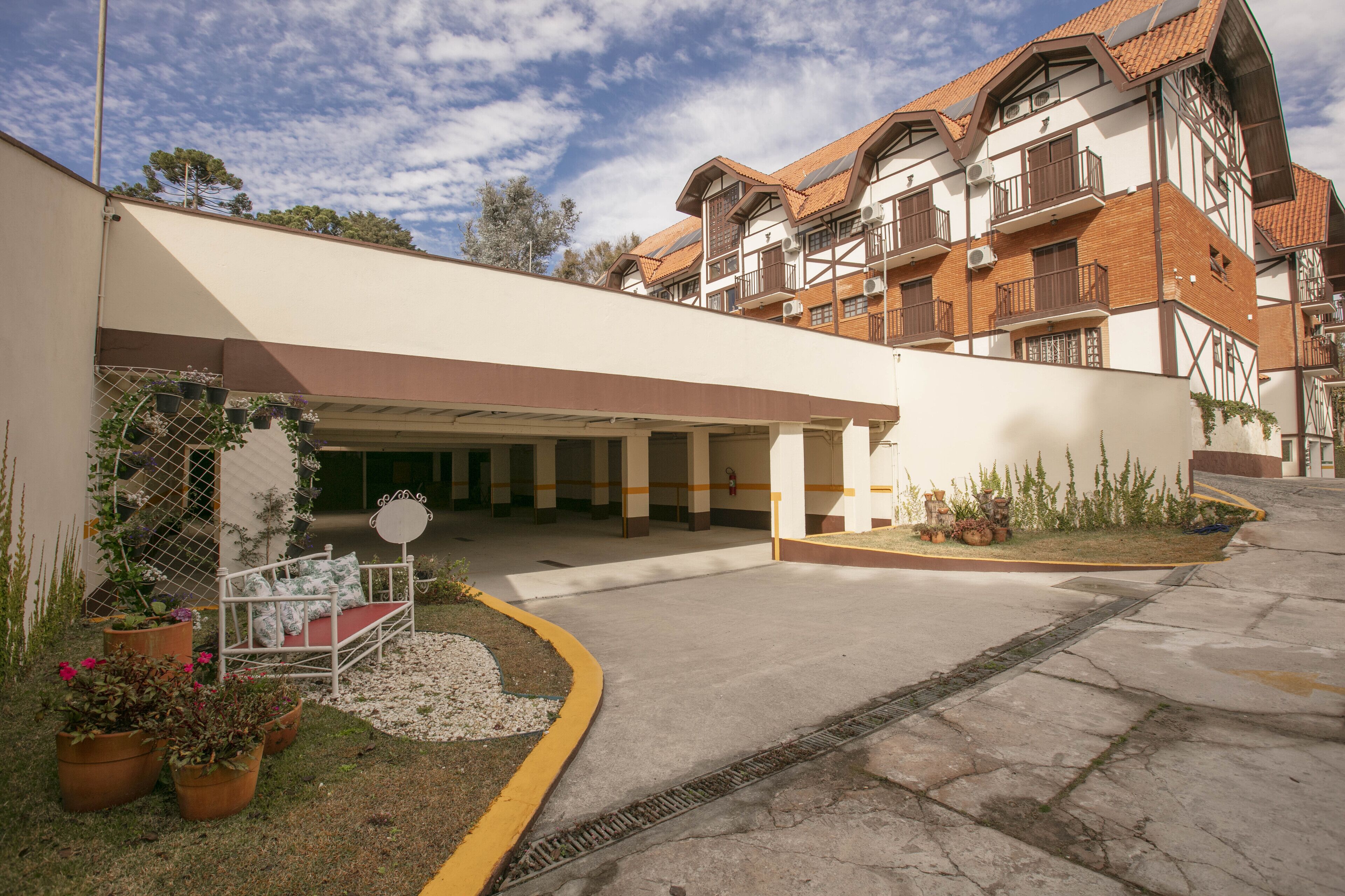 A hotel entrance with a covered waiting area, outdoor seating, and potted plants.
