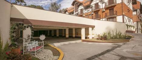A hotel entrance with a covered waiting area, outdoor seating, and potted plants.