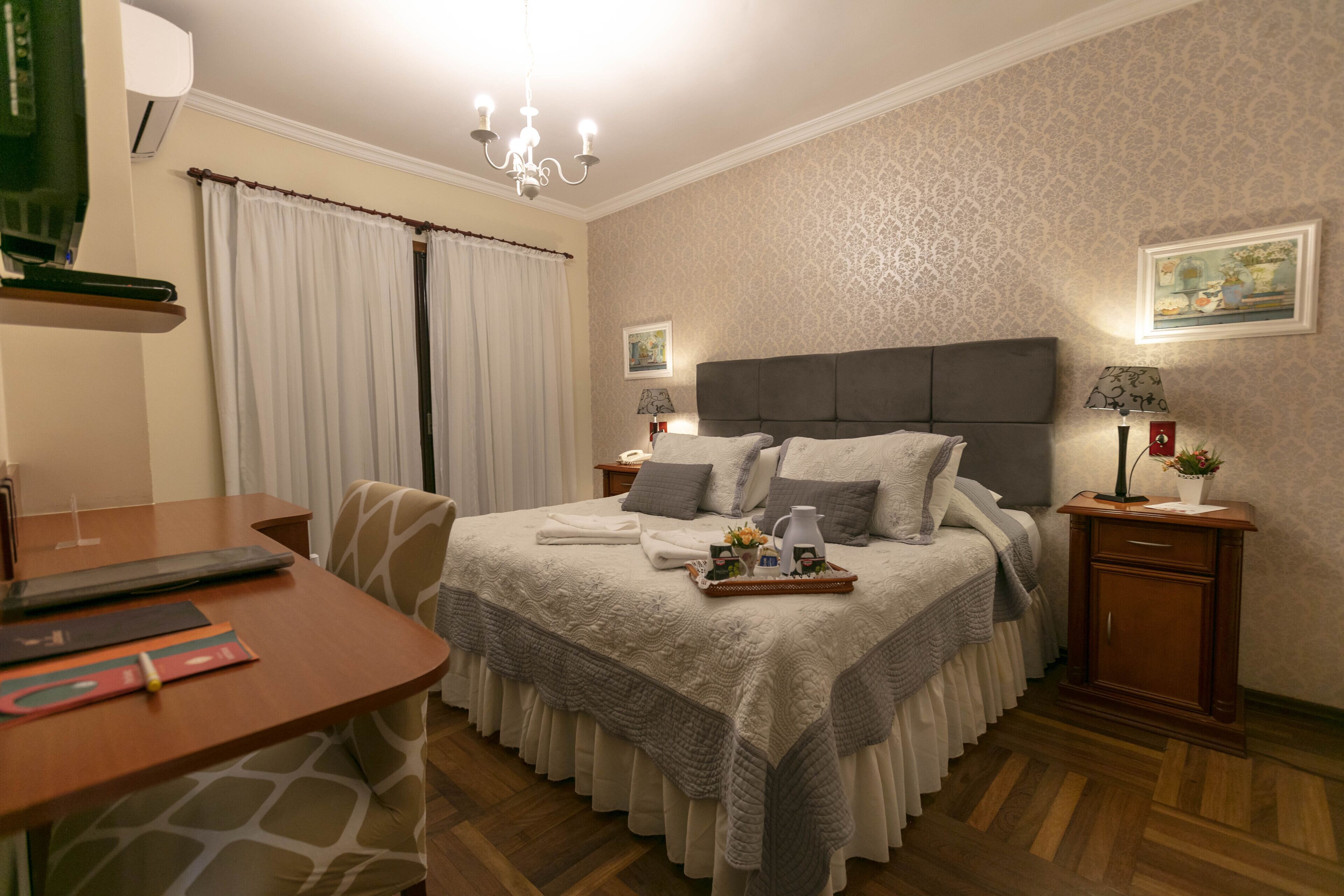 A neatly arranged bedroom with a bed, bedside tables, a desk, and a chair.
