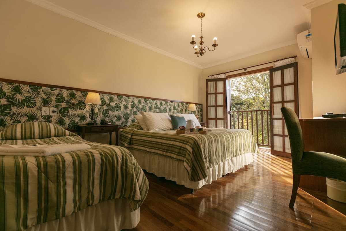 A bedroom with two beds, a wooden floor, a chandelier, and a view of the outdoors.