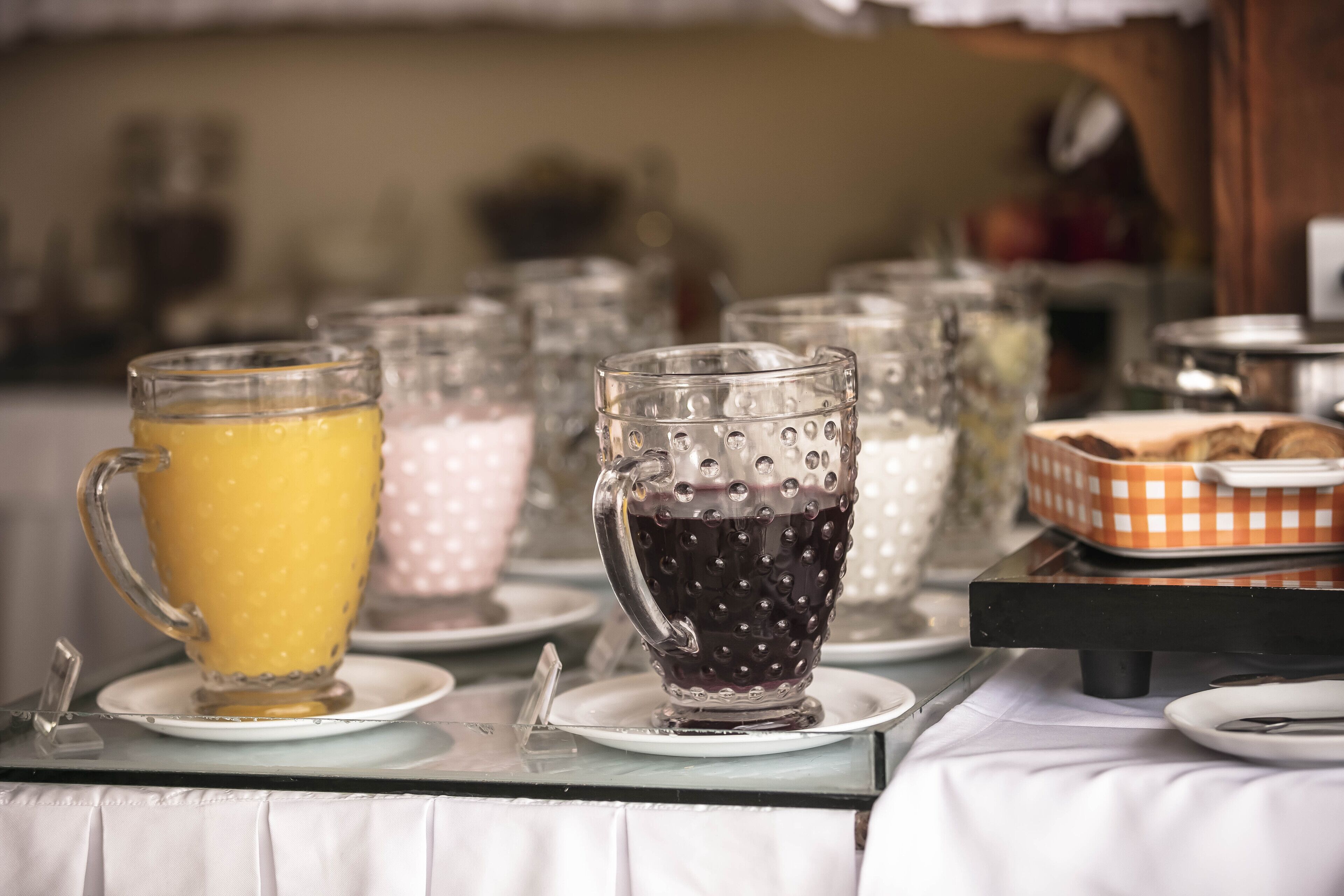 A breakfast table with clear glass cups, a basket of pastries, and a fruit bowl.