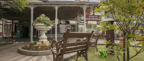 Un jardín con un banco, una fuente y un edificio con un cartel.