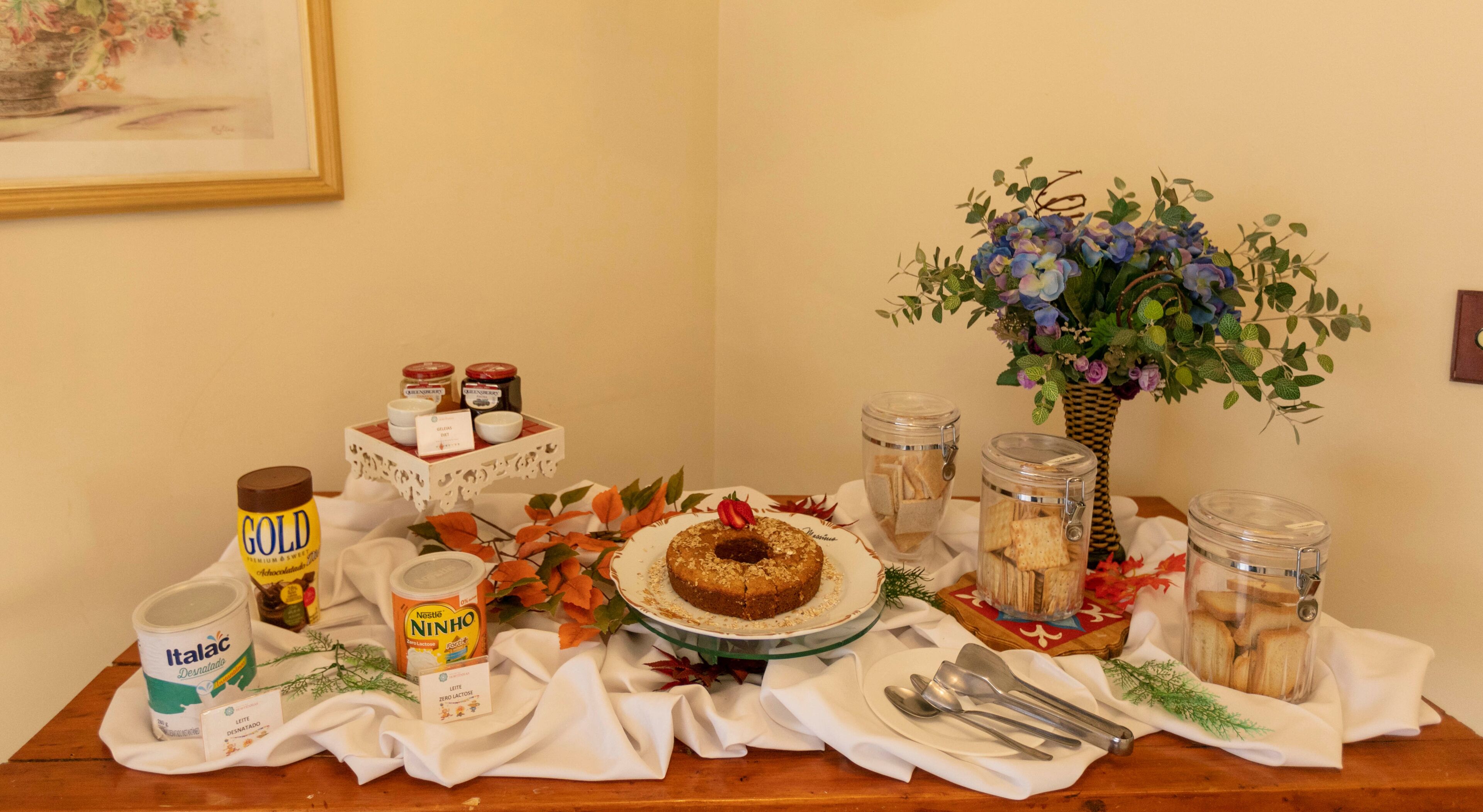 Una mesa con un pastel, botes de galletas y un jarrón de flores.