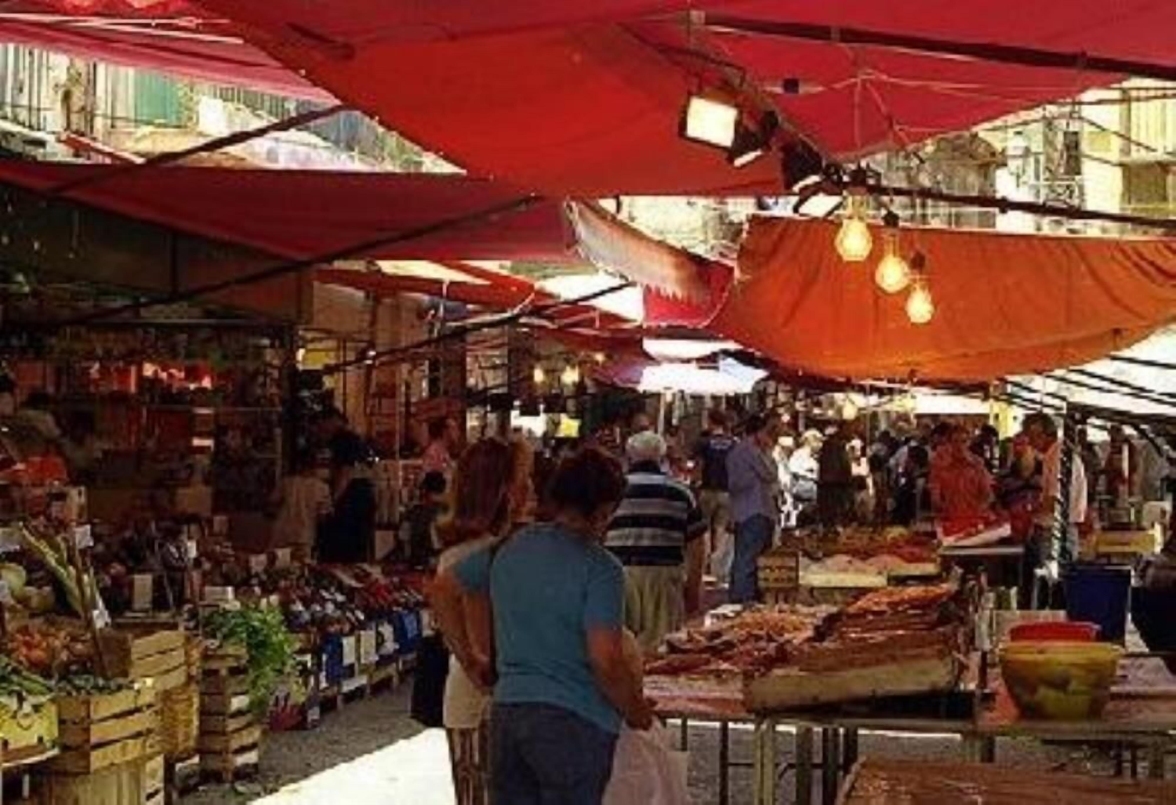 Um mercado ao ar livre com diversos quiosques e pessoas a fazer compras.