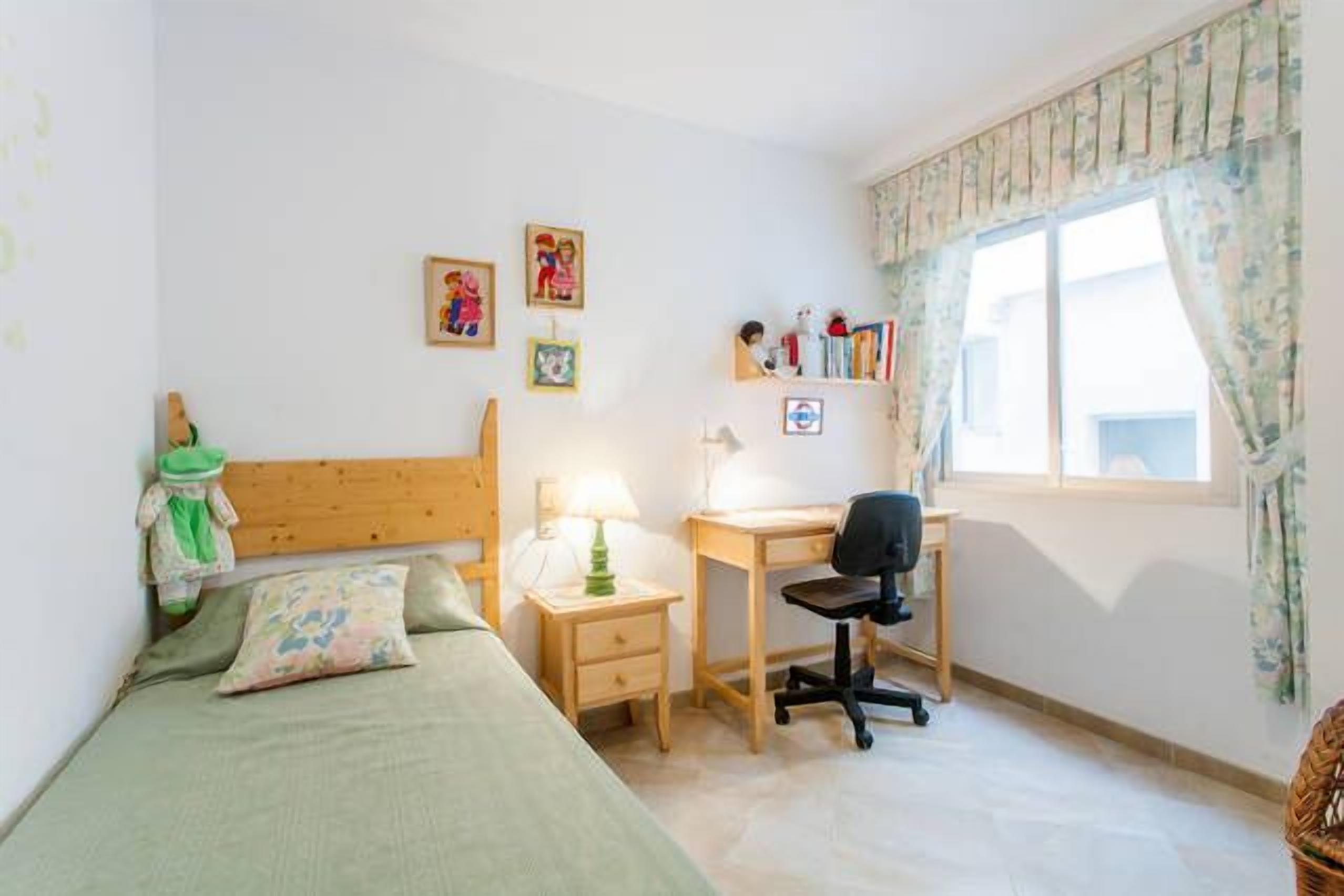 A bedroom with a bed, a desk, a chair, and a window with curtains.
