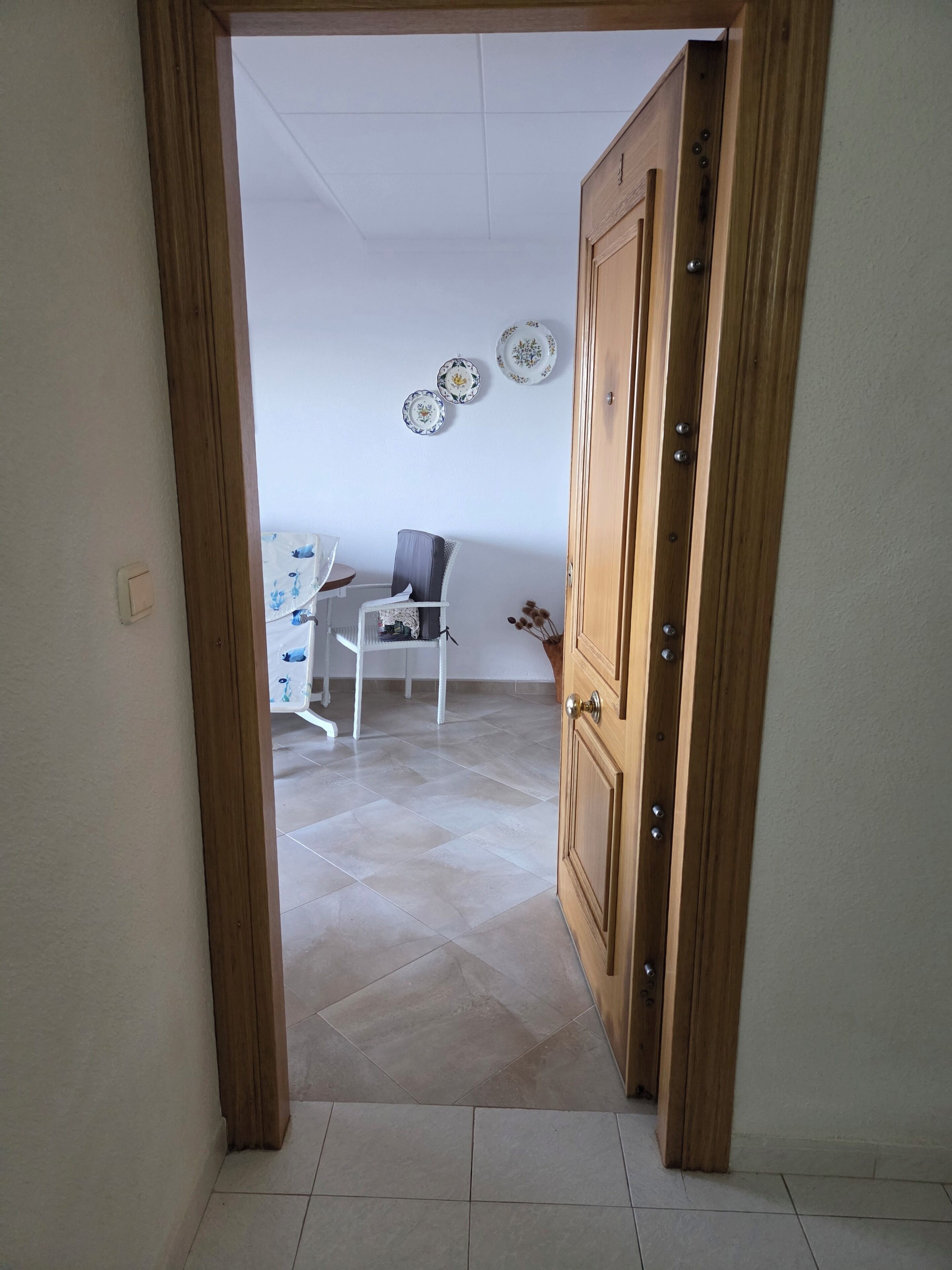 Une pièce avec une porte en bois, une chaise blanche, une petite table et un mur orné d’assiettes décoratives.