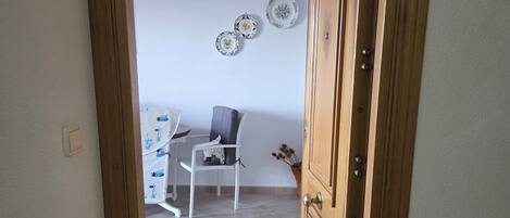 Une pièce avec une porte en bois, une chaise blanche, une petite table et un mur orné d’assiettes décoratives.