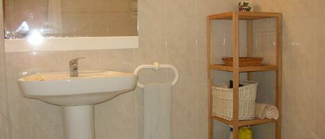 A bathroom with a sink, a mirror, a shower, and a wooden shelf with baskets.