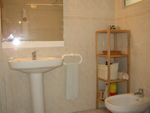 A bathroom with a sink, a mirror, a shower, and a wooden shelf with baskets.