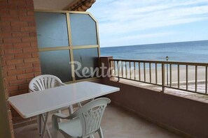 A balcony with a white table and chairs, a view of the beach, and a brick wall.