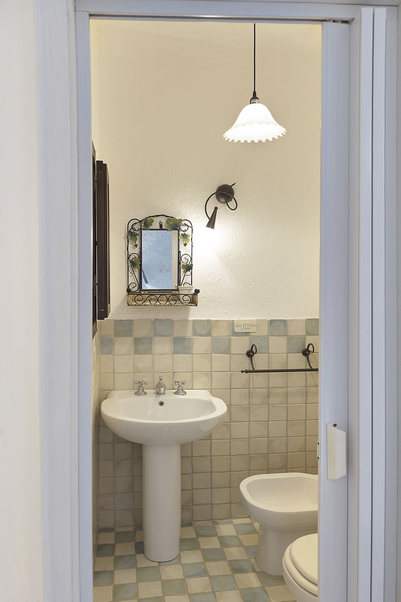 Ein Badezimmer mit einem weißen Waschbecken, einer Toilette und einem Spiegel mit dekorativem Rahmen.