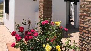 Un edificio blanco con una chimenea de ladrillo, un farol negro y un jardín con flores rojas y amarillas.