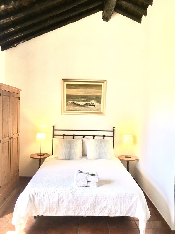 A neatly made bed with a white bedspread, two bedside lamps, and a framed painting above. - Beautiful Country House with Pool and Scenic Mountain Views (Ronda)