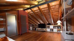 A spacious loft with a high ceiling, wooden beams, a television, a bookshelf, and a white sofa.