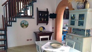 A dining area with a table set for two, a wooden staircase, and a kitchen area with cabinets and a television. - The House between Sea and Nature  (Custonaci)
