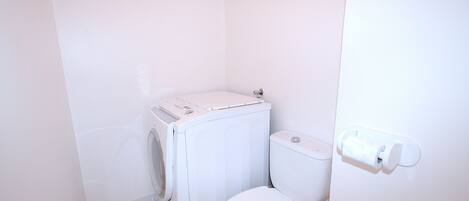 Une petite salle de bain aux murs blancs, équipée d’un lave-linge et de toilettes.