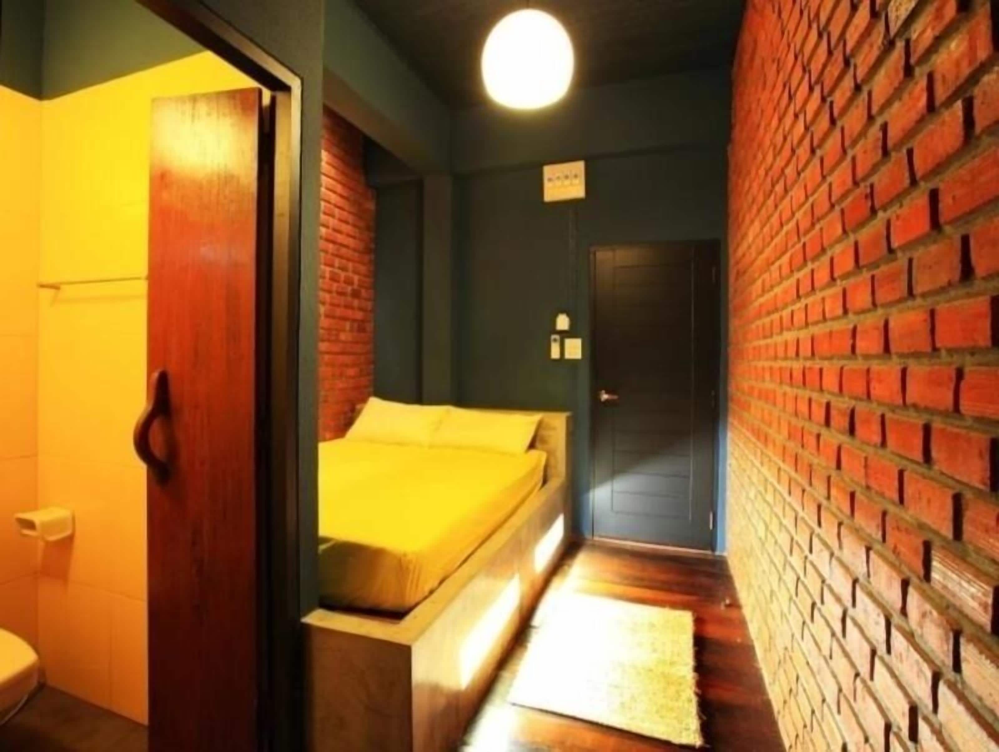 Un corridoio stretto con un letto in fondo, una porta e un muro in mattoni.