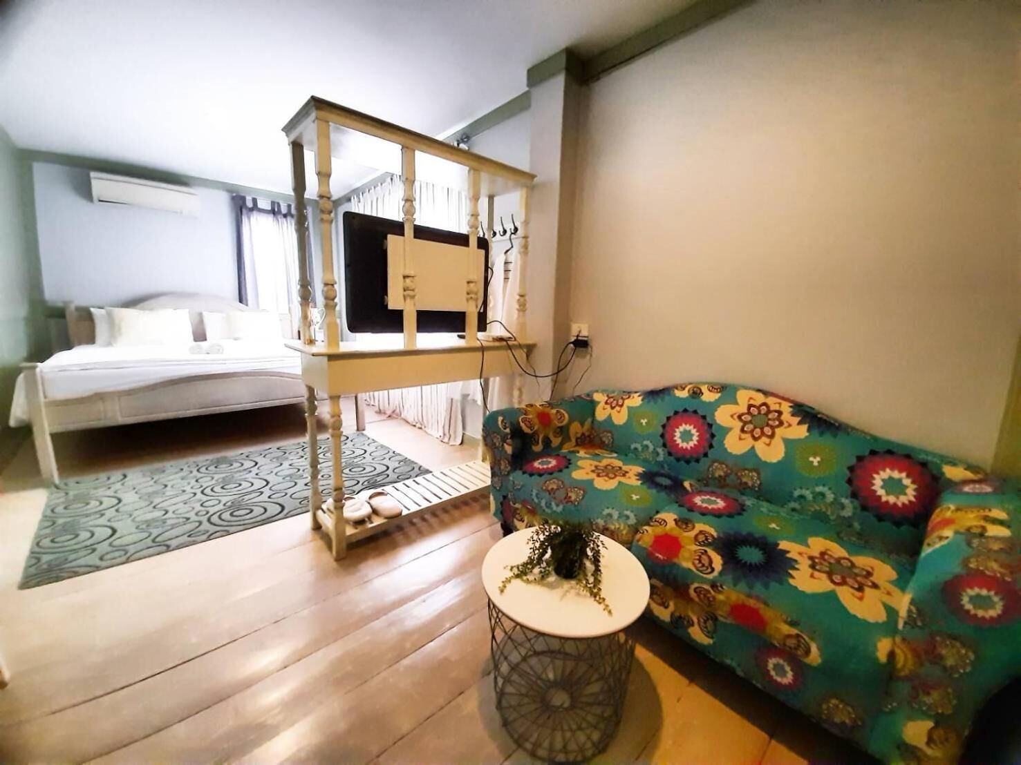 Een kamer met een bed, een kleurrijke bank, een kleine ronde tafel en een houten tv-meubel.