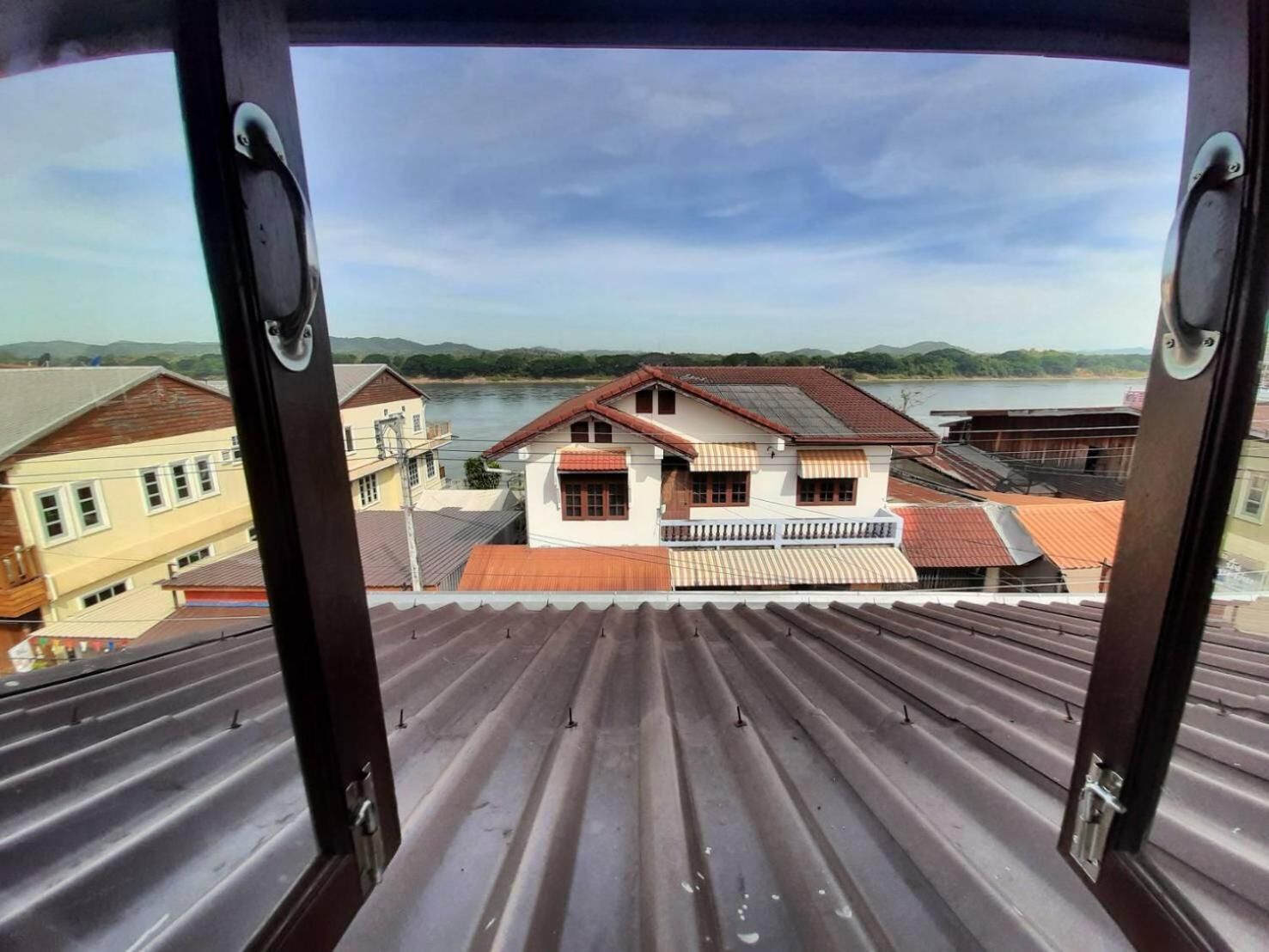 A view from a window overlooking a river and buildings with a corrugated metal roof.