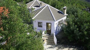 Un bâtiment blanc, doté d’un toit en tuiles, entouré de verdure et de collines.