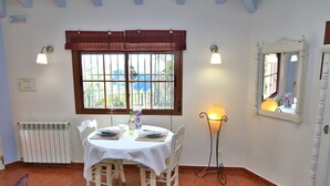 Un coin repas avec une table dressée pour quatre personnes, un radiateur, une fenêtre donnant sur un beau paysage et un lampadaire.